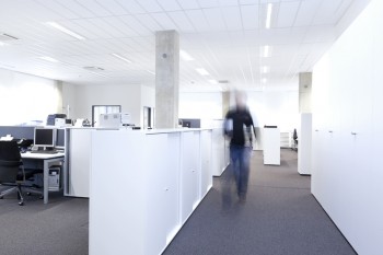 Helles Büro mit weißen Möbeln und einer gehenden Person in Bewegungsunschärfe